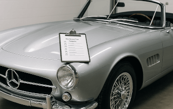 An illustration of the essential steps for preparing a classic car for long-term storage, including using jack stands, a battery tender, fuel stabilizer, and a breathable cover to preserve its condition.